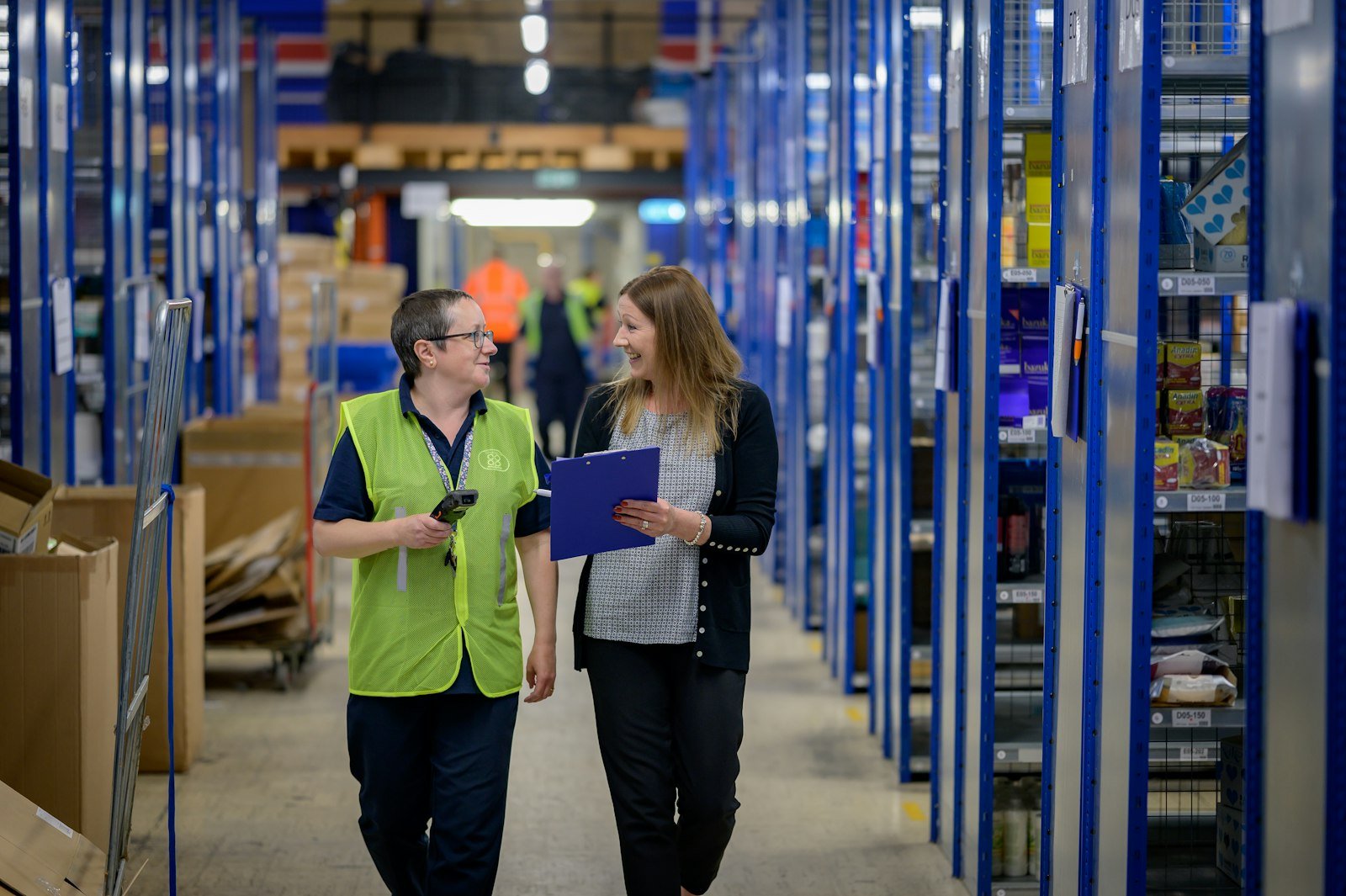 Two people walking down a warehouse aisle lined with shelves