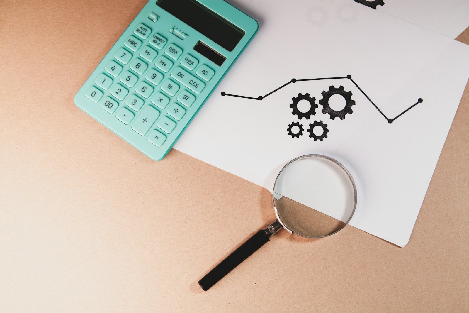 Calculator, magnifying glass, and a chart with gears on paper