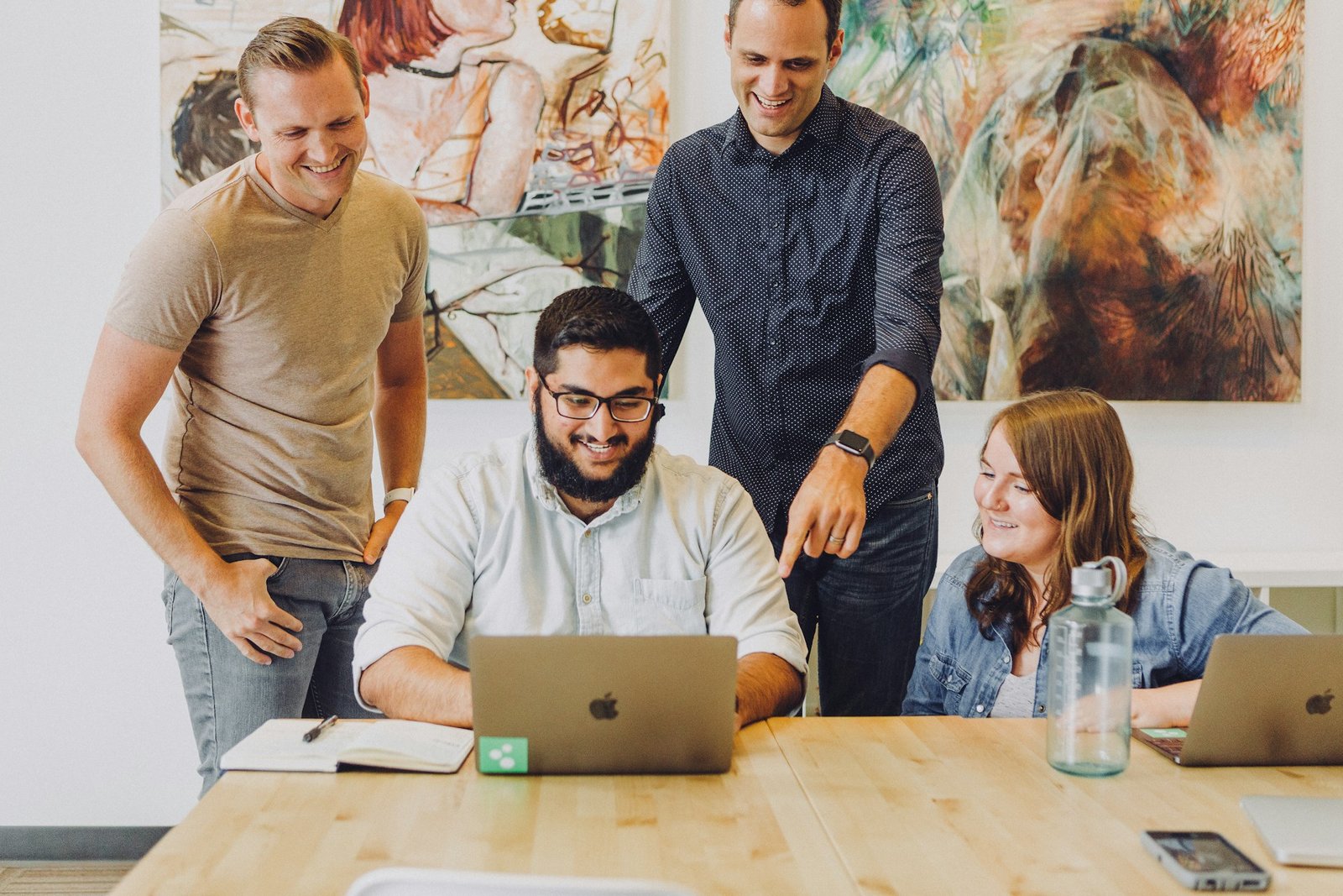Team of four coworkers collaborating around a laptop, representing unlimited users on Xero plans