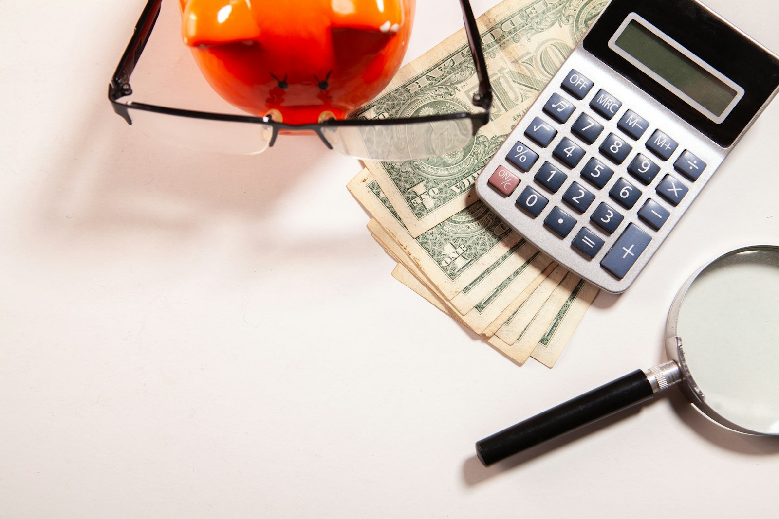 Calculator, magnifying glass, and money on a white surface