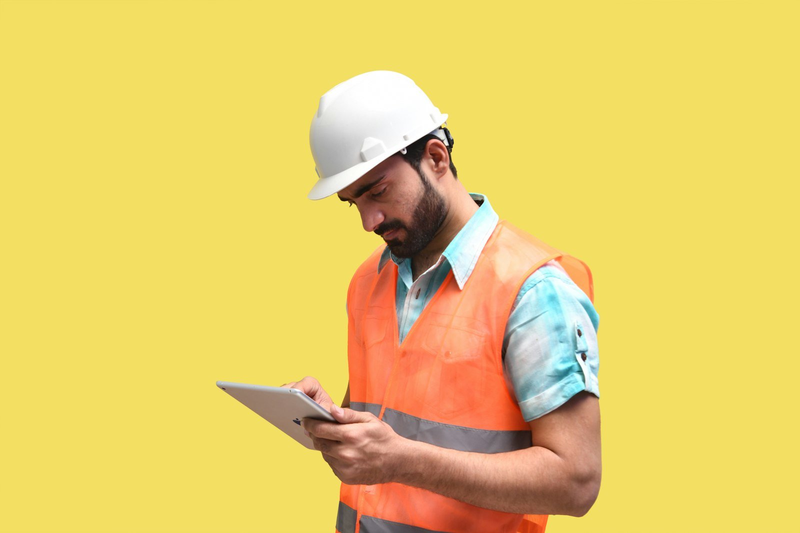 Person wearing a hard hat and looking at a tablet on a job site