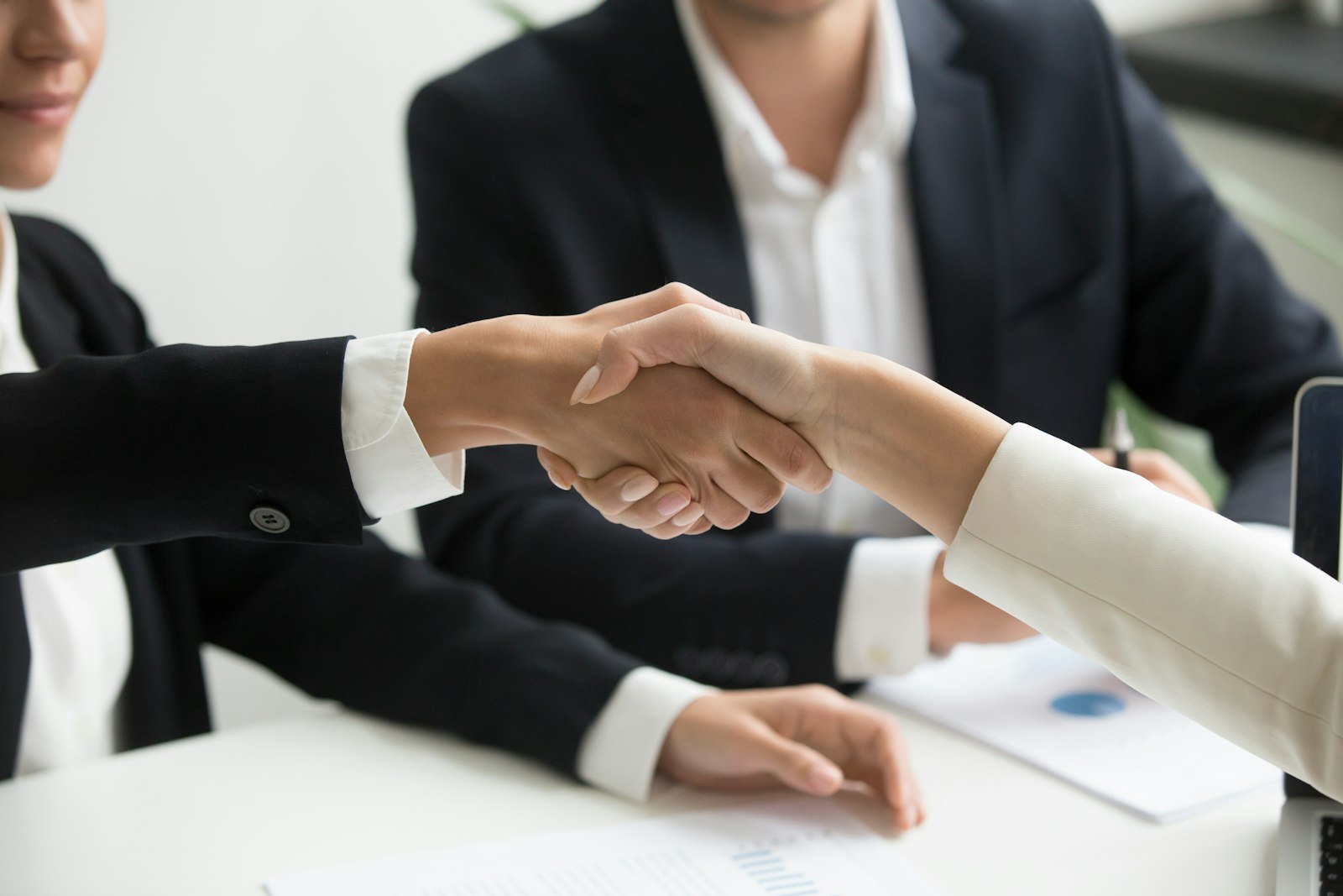 Two people shaking hands in front of a laptop, representing a business partnership